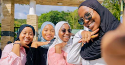 A group of 4 girls are posing for a selfie, smiling at the camera.